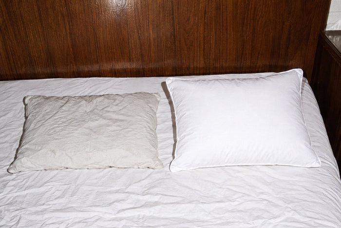 En gammal platt kudde bredvid en ny A Funky Dream-kudde i en hotellsäng