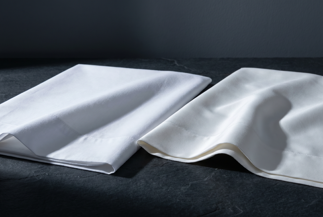 Matt vitt percale och lystrande Supimabomull på en mörk stenyta i sidoljus